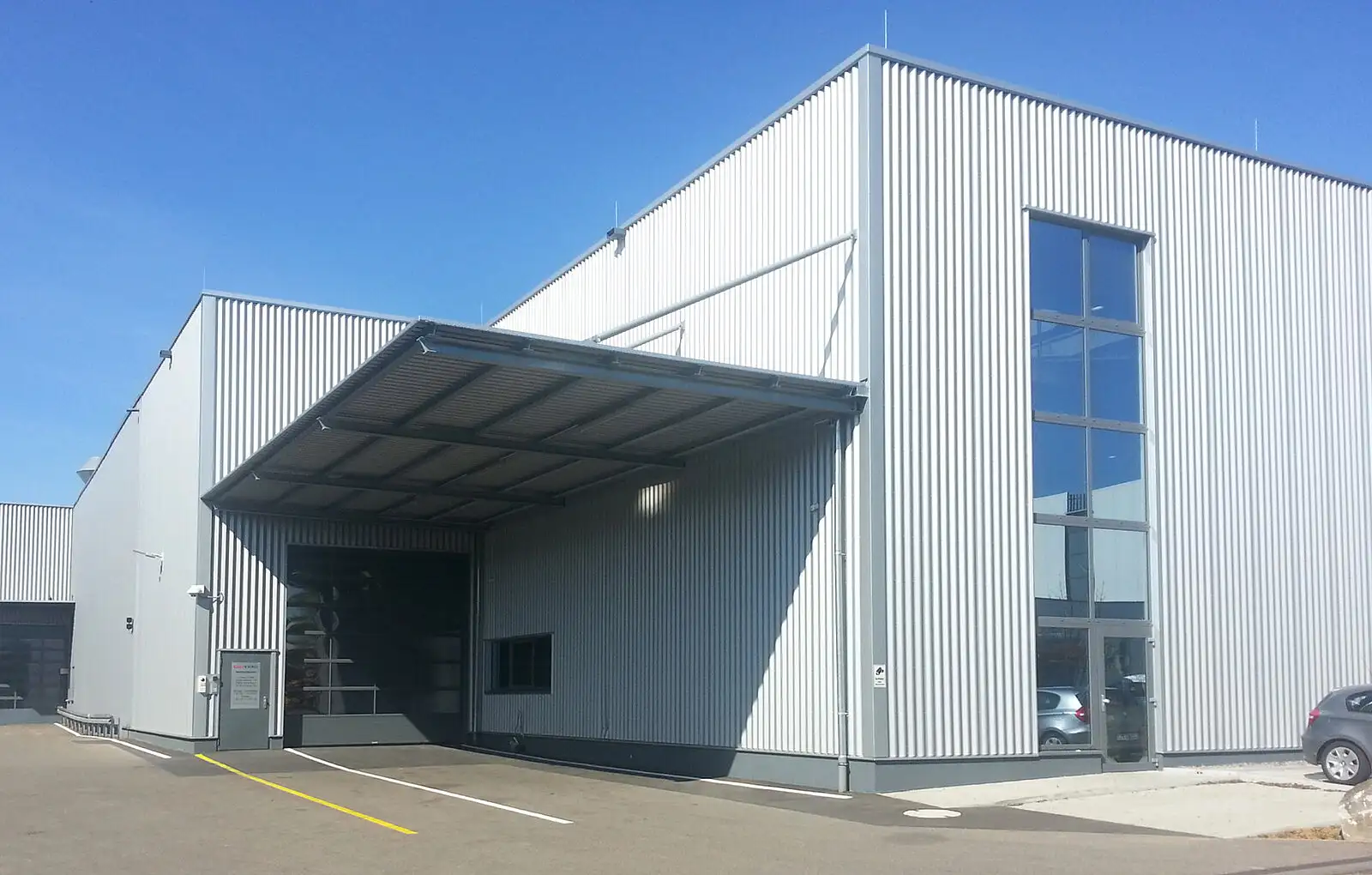 Moderne Industriehalle von PUR Projektbau mit grauem Rolltor und Vordach im Außenbereich