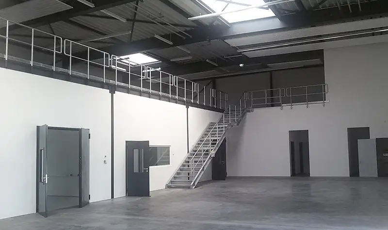 Innenansicht einer leeren Gewerbehalle mit einer Treppe, die auf eine Empore führt.