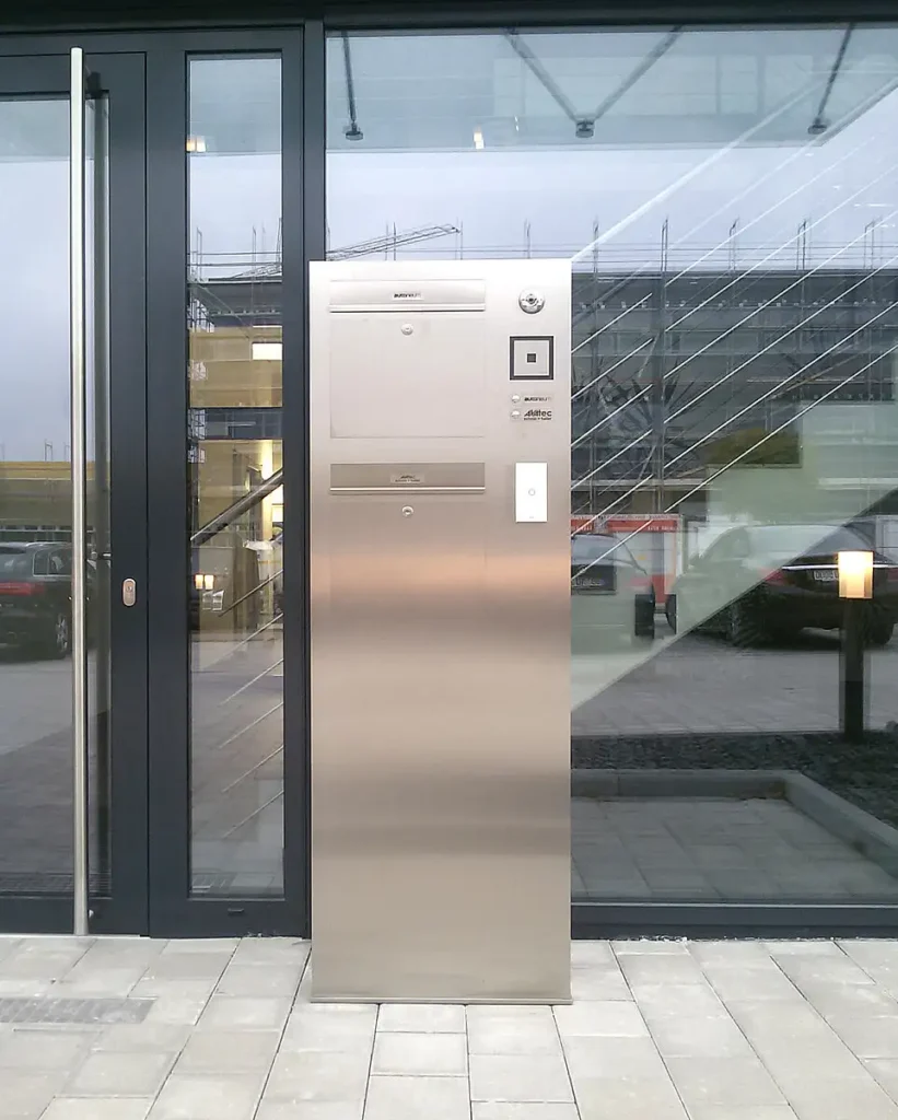 Moderne Edelstahl-Kommunikationsstele vor dem Eingang eines PUR Projektbau Gebäudes.