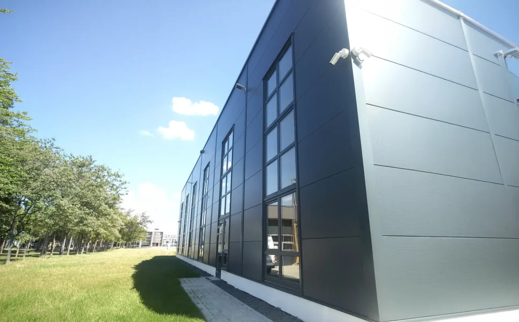 Seitliche Perspektive eines Industriegebäudes mit moderner Profilblech-Fassade im Sonnenlicht.