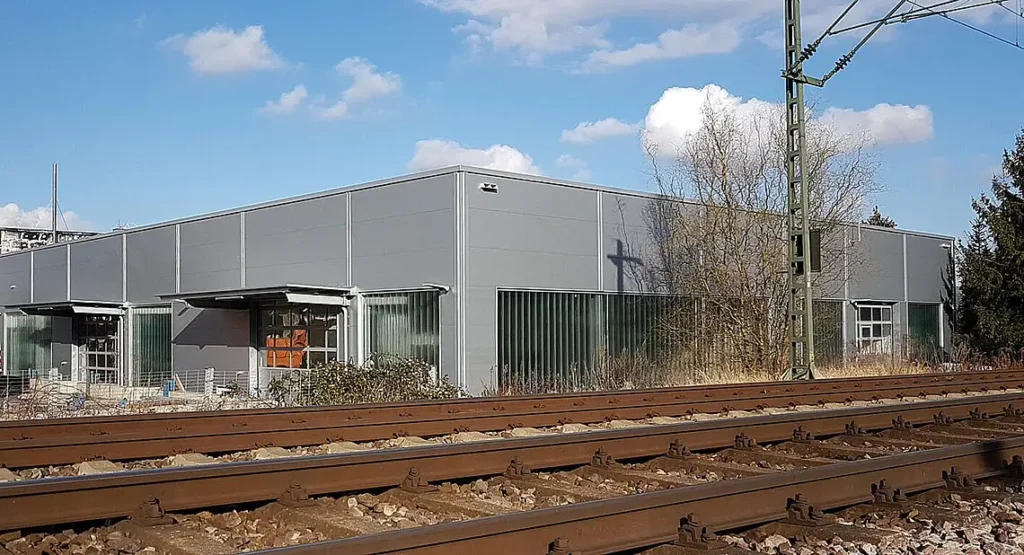 Außenansicht eines grauen Industriegebäudes direkt an einer Bahnschiene.