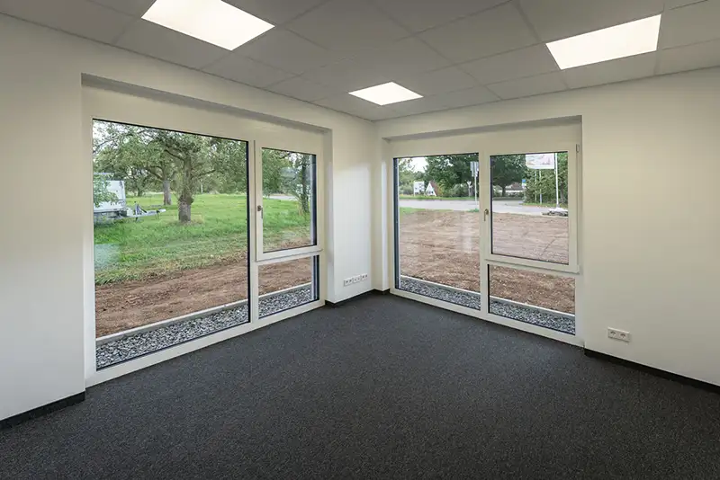 Innenansicht eines leeren Büros mit großen Fensterfronten und Blick ins Grüne.