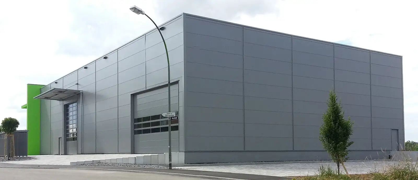 Außenansicht einer minimalistischen, grauen Industriehalle mit Straßenlaterne.