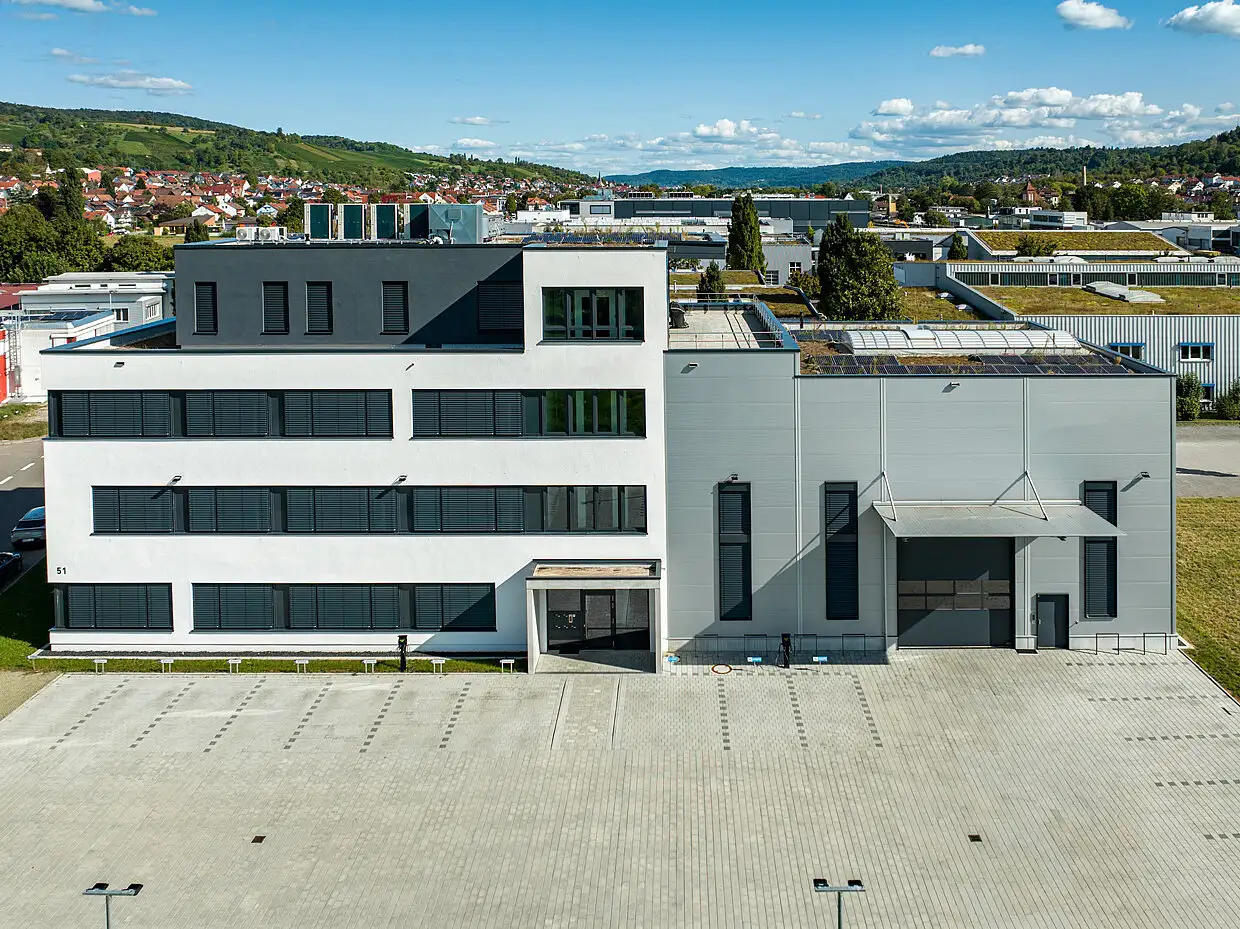 Frontale Ansicht eines minimalistischen Industriegebäudes mit weißem Verwaltungstrakt und grauer Gewerbehalle.