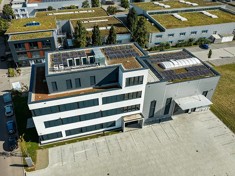 Vogelperspektive auf einen modernen Bau-Komplex bestehend aus Verwaltung und Gewerbehalle mit Gründach-Elementen.