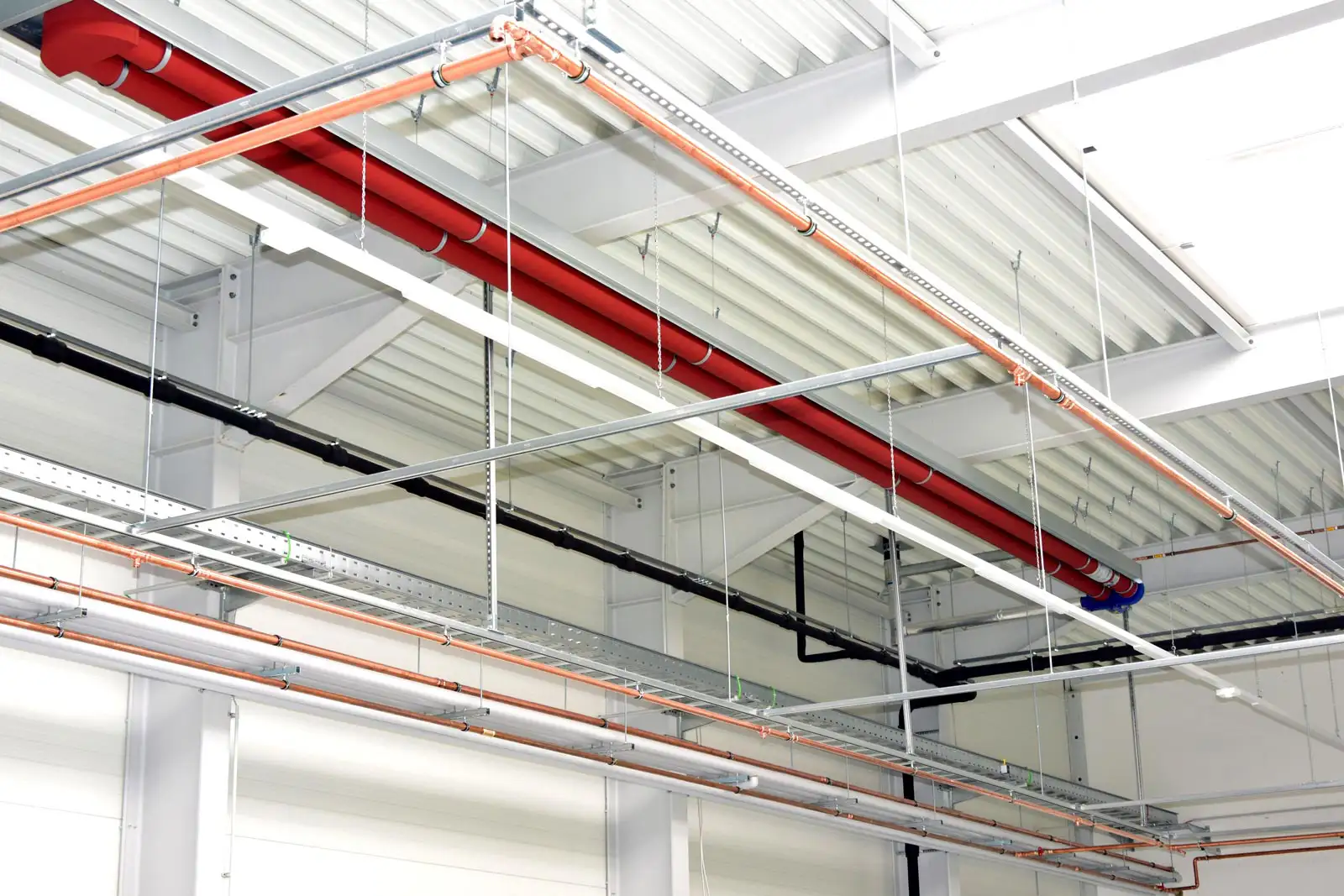 Sichtbare Rohrleitungen und Sprinkleranlagen an der Decke einer Industrie-Produktionshalle.