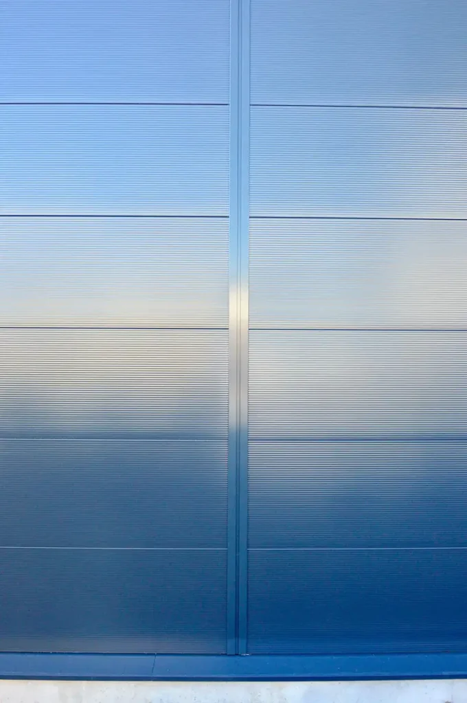 Nahaufnahme einer modernen, blau-grau schimmernden Metallfassade aus Sandwichpaneelen an einer Industriehalle von PUR Projektbau.
