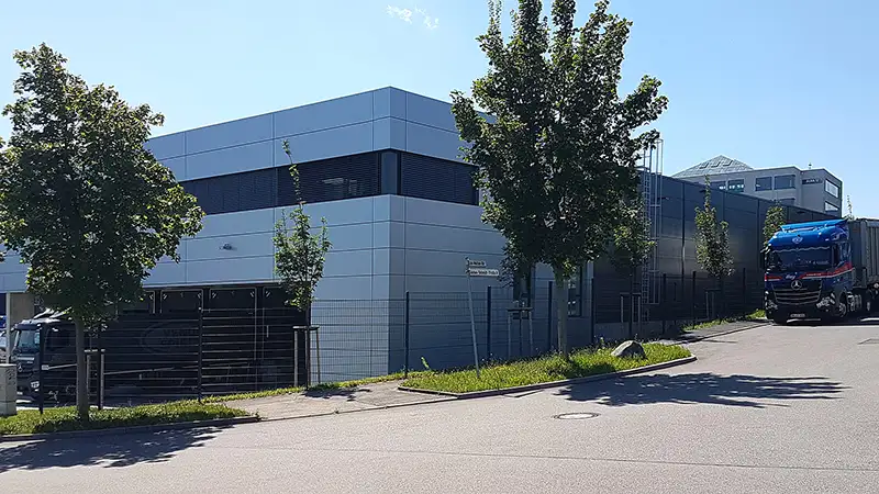 Außenansicht eines minimalistischen, dunkelgrauen Gewerbegebäudes mit Parkplatz.
