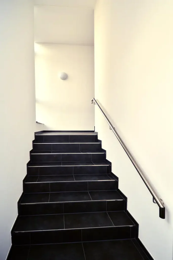 Moderne, dunkle Steintreppe mit Edelstahlgeländer im Innenbereich eines Gewerbebaus.