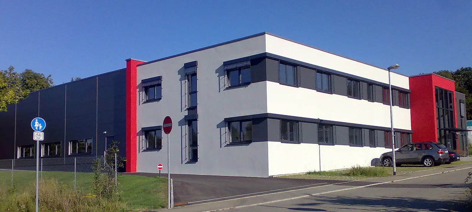 Modernes Industriegebäude mit weißen Fassadenelementen und roten Akzenten von PUR Projektbau.