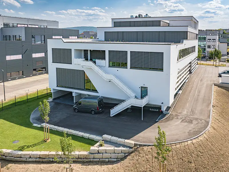 Modernes, weißes Gewerbe-Gebäude mit Außentreppe und gepflegten Außenanlagen.