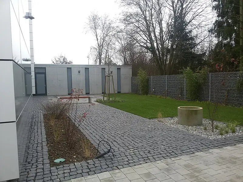 Modern gestaltete Außenanlage eines Bürogebäudes mit Steinplatten und Rasen.
