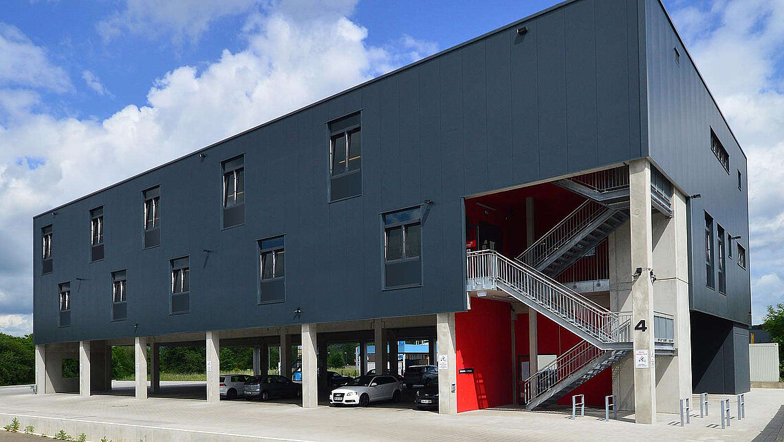 Anthrazitfarbenes Fitnessgebäude mit roten Akzenten an der Außentreppe von PUR Projektbau.