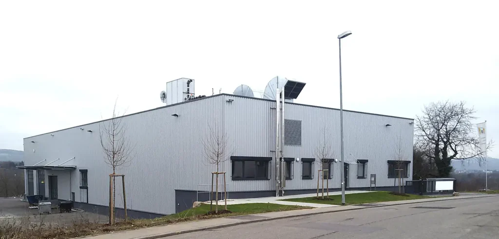 Außenansicht eines langgezogenen, weißen Industriegebäudes mit Flachdach.