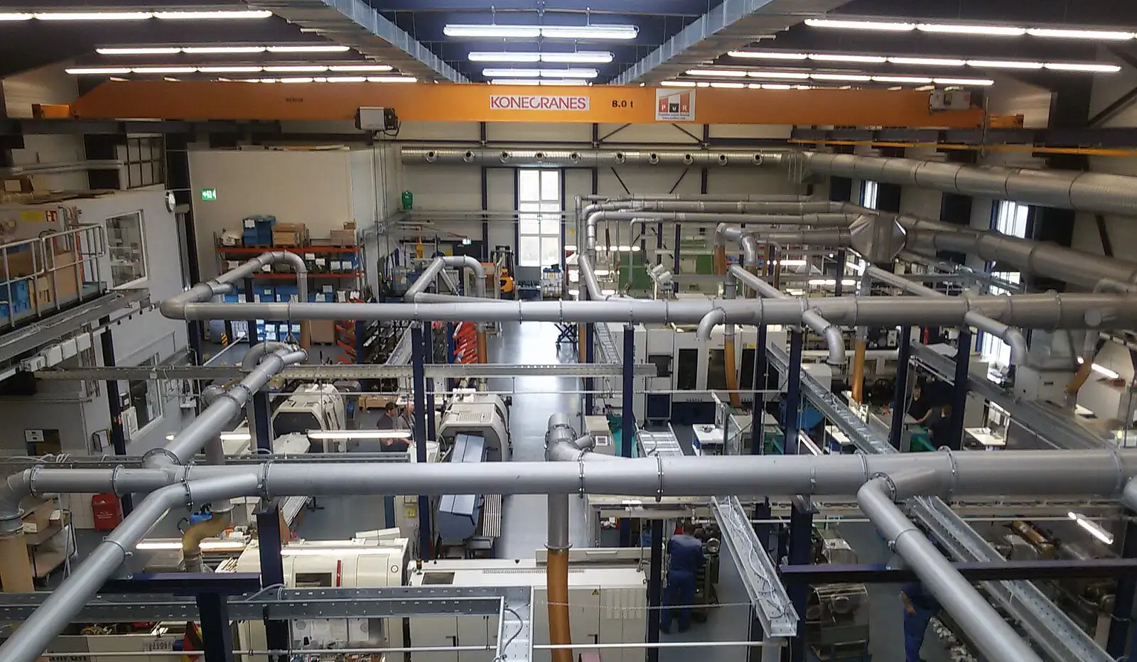 Blick in eine Industriehalle mit komplexen Rohrleitungen und technischer Ausstattung an der Decke.