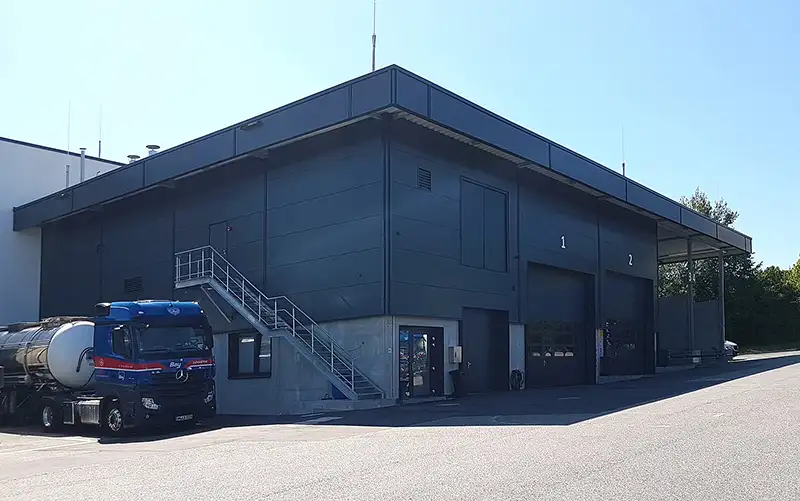Dunkle Außenfassade einer modernen Industriehalle unter blauem Himmel.