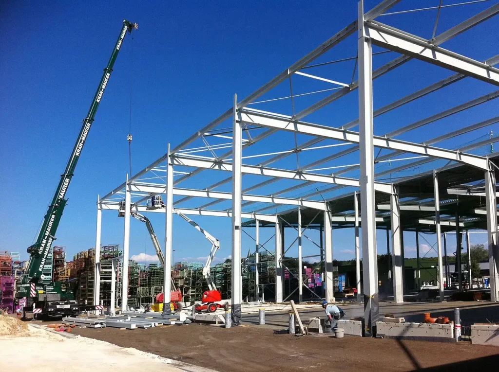 Baustelle einer Gewerbehalle mit aufgestelltem Stahltragwerk unter blauem Himmel.