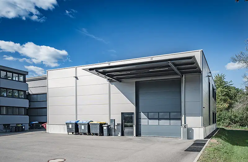 Großes graues Rolltor und überdachter Verladebereich an einer modernen Produktions- und Lagerhalle.