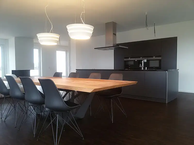 Moderner Aufenthaltsraum mit Küche in einem PUR Projektbau Gebäude mit großem Holztisch.