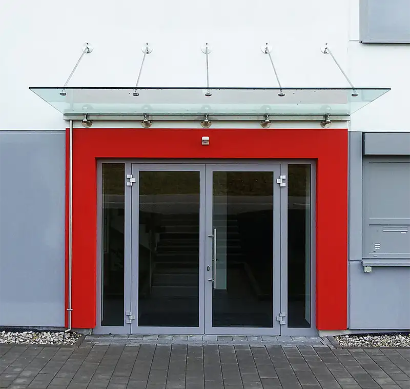 Moderner Haupteingang eines Bürogebäudes mit rotem Rahmen und Glasvordach.