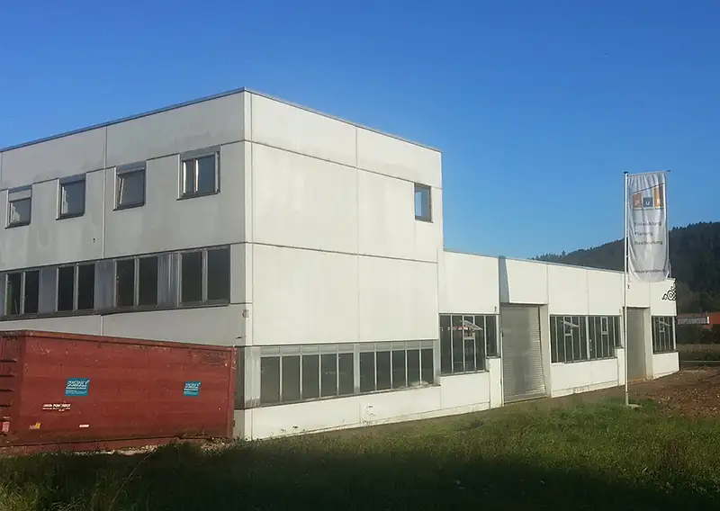 Eckansicht eines kubischen, weißen Gewerbegebäudes unter blauem Himmel.